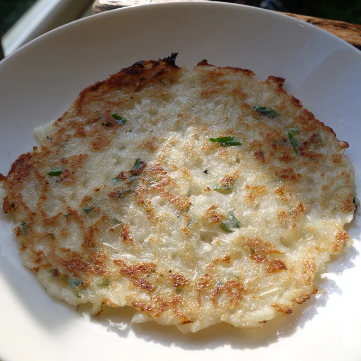 Golden-brown Irish Boxty potato pancakes studded with fresh scallions rest on a rustic plate, their crispy edges contrasting with a soft, fluffy interior.  