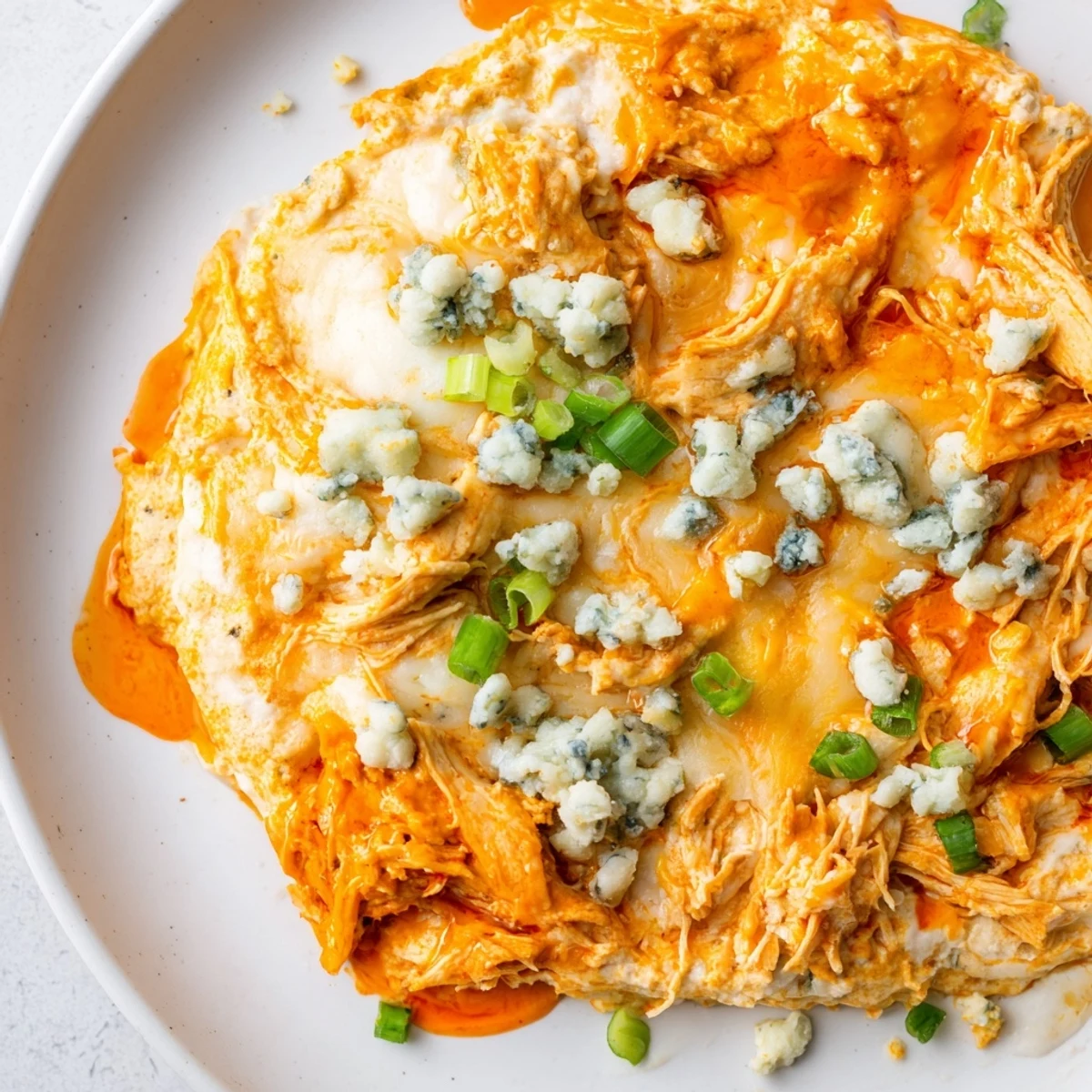 A scoop of cheesy Keto Buffalo Chicken Dip on a low carb cracker, with buffalo sauce and shredded chicken visible.