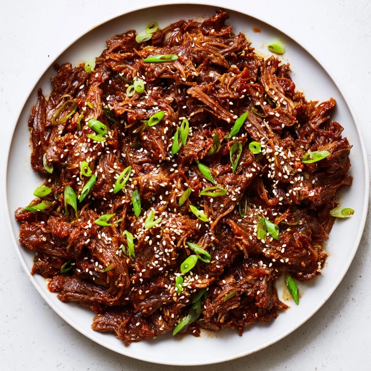 Tender shredded Slow Cooker Korean Beef simmered in a savory-sweet sauce, served over fluffy white rice with green onions.  