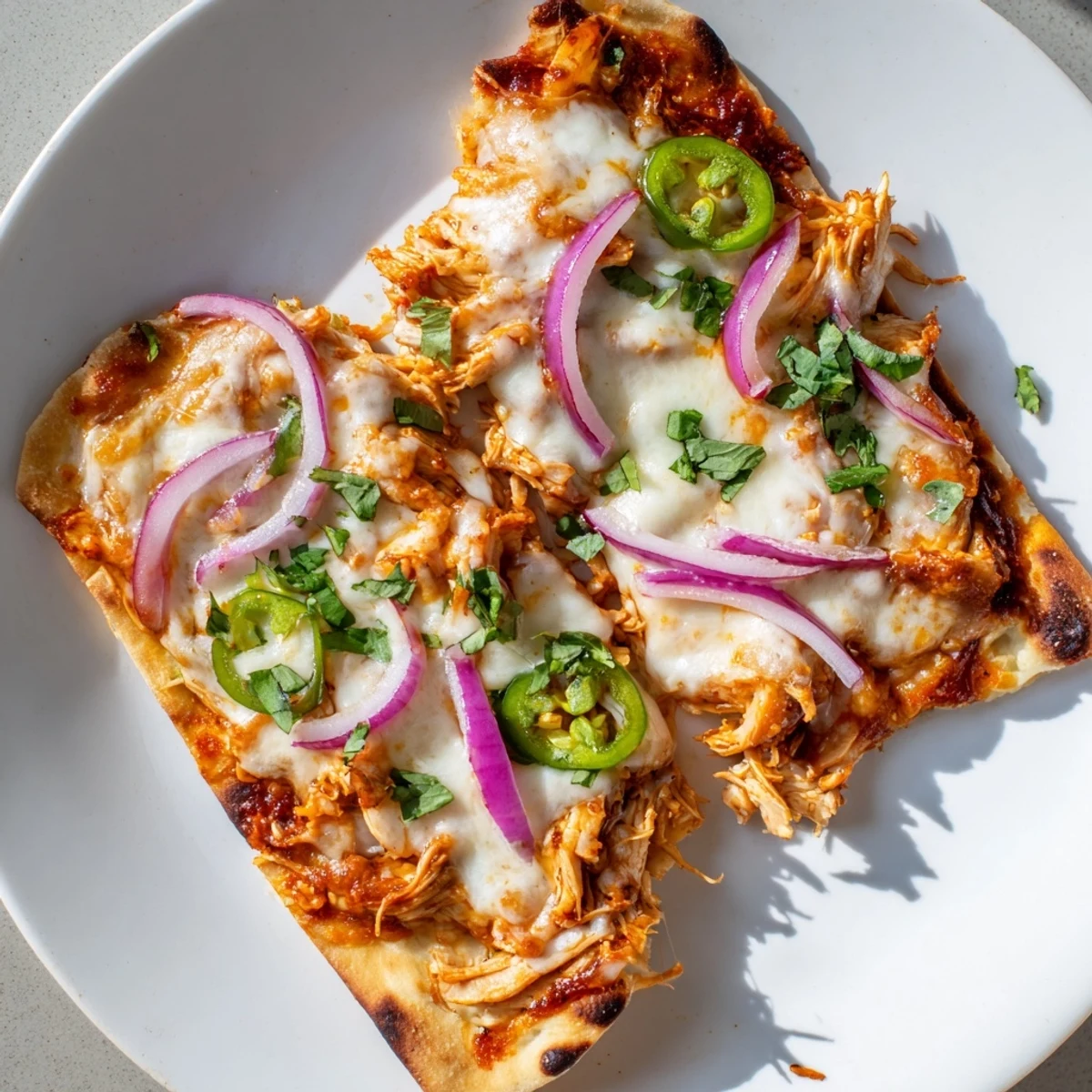 Freshly baked BBQ Chicken Flatbread with melty mozzarella and cheddar, topped with red onions and cilantro on a wooden board.