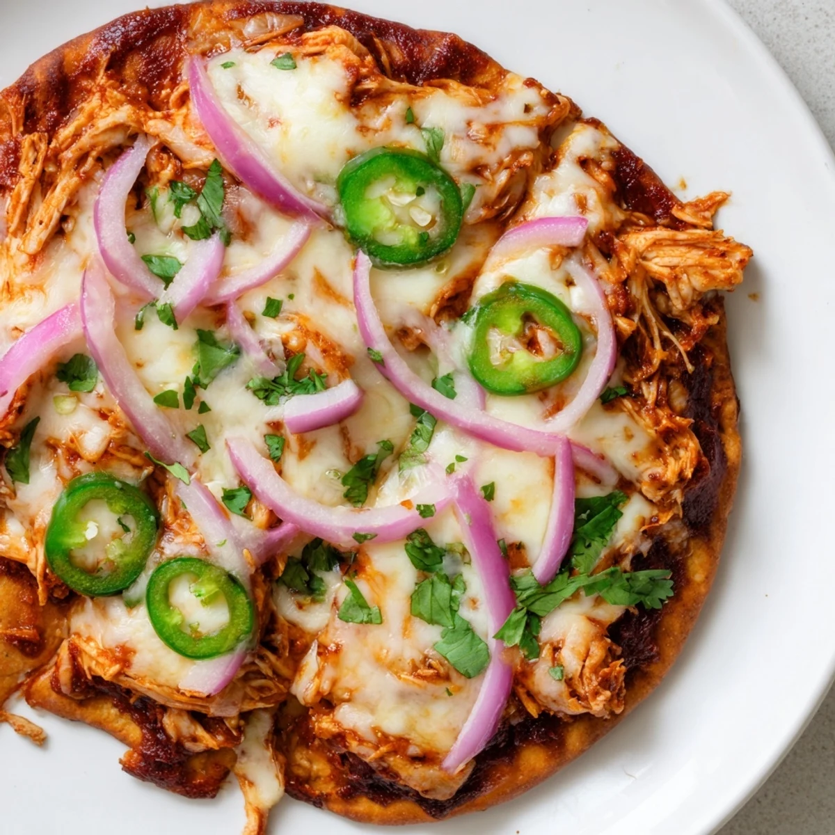 Homemade BBQ Chicken Flatbread on a baking sheet, featuring juicy shredded chicken, melted cheese, and vibrant red onions and jalapeños.