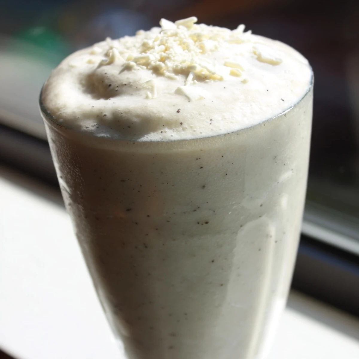 A frosty blended Vanilla Bean Frappuccino with visible vanilla bean speckles beside a straw and ice.