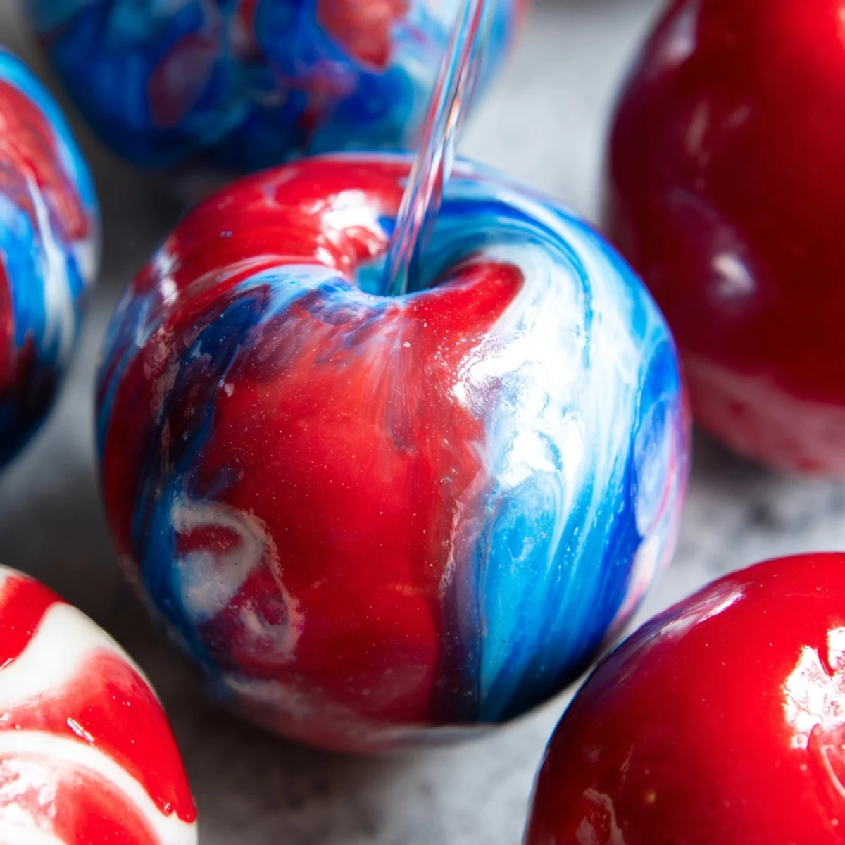 Eight glossy Marbled Effect Candy Apples rest on parchment, their vibrant swirled red, blue, and white shells glistening under studio lighting.