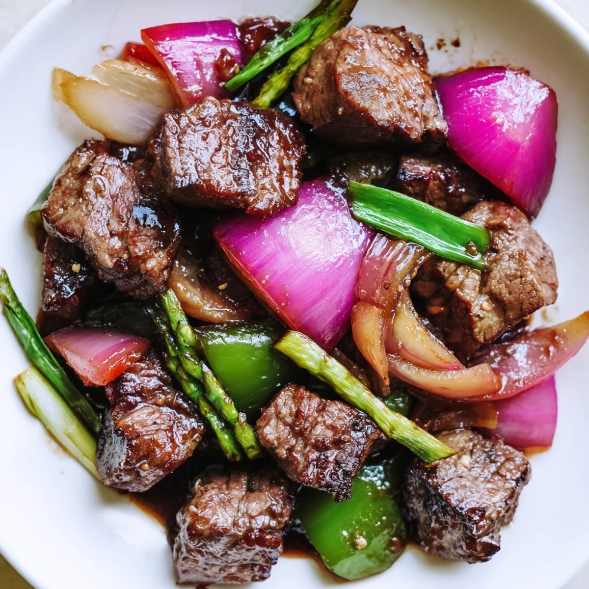 Vietnamese Shaking Beef features seared steak, crisp peppers, and onions on a bed of greens.