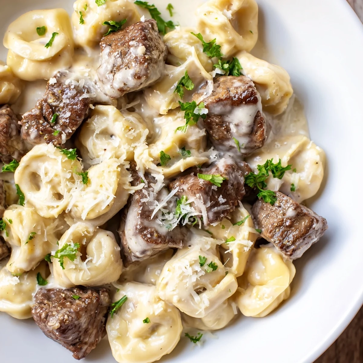A fork lifts tender steak and tortellini coated in a creamy garlic sauce, with steam rising above the skillet.