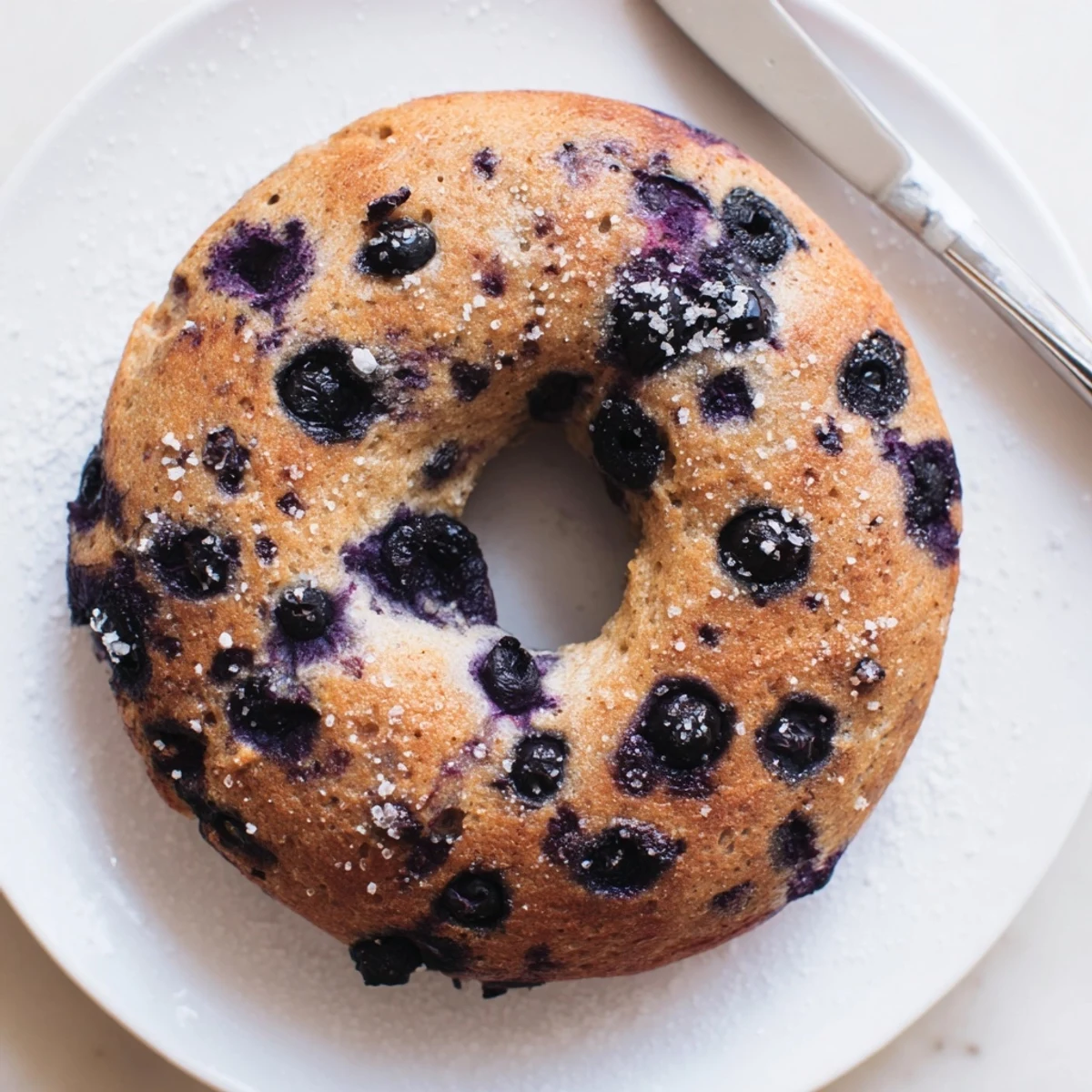 Freshly baked gluten-free blueberry bagels cooling on a wire rack with glistening blueberries inside.
