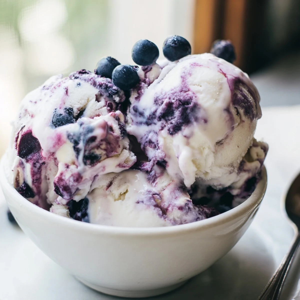 A bowl of creamy homemade Blueberry Cottage Cheese Ice Cream with vibrant blueberry swirls on a wooden table.