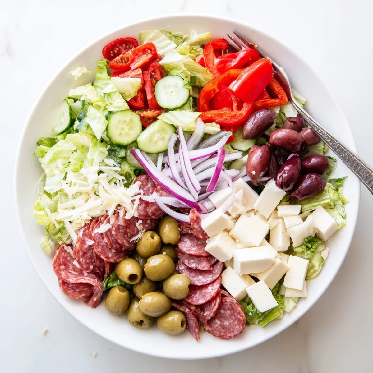 Colorful Italian chopped salad with fresh vegetables, salami, cheese cubes, and zesty homemade dressing in a bowl