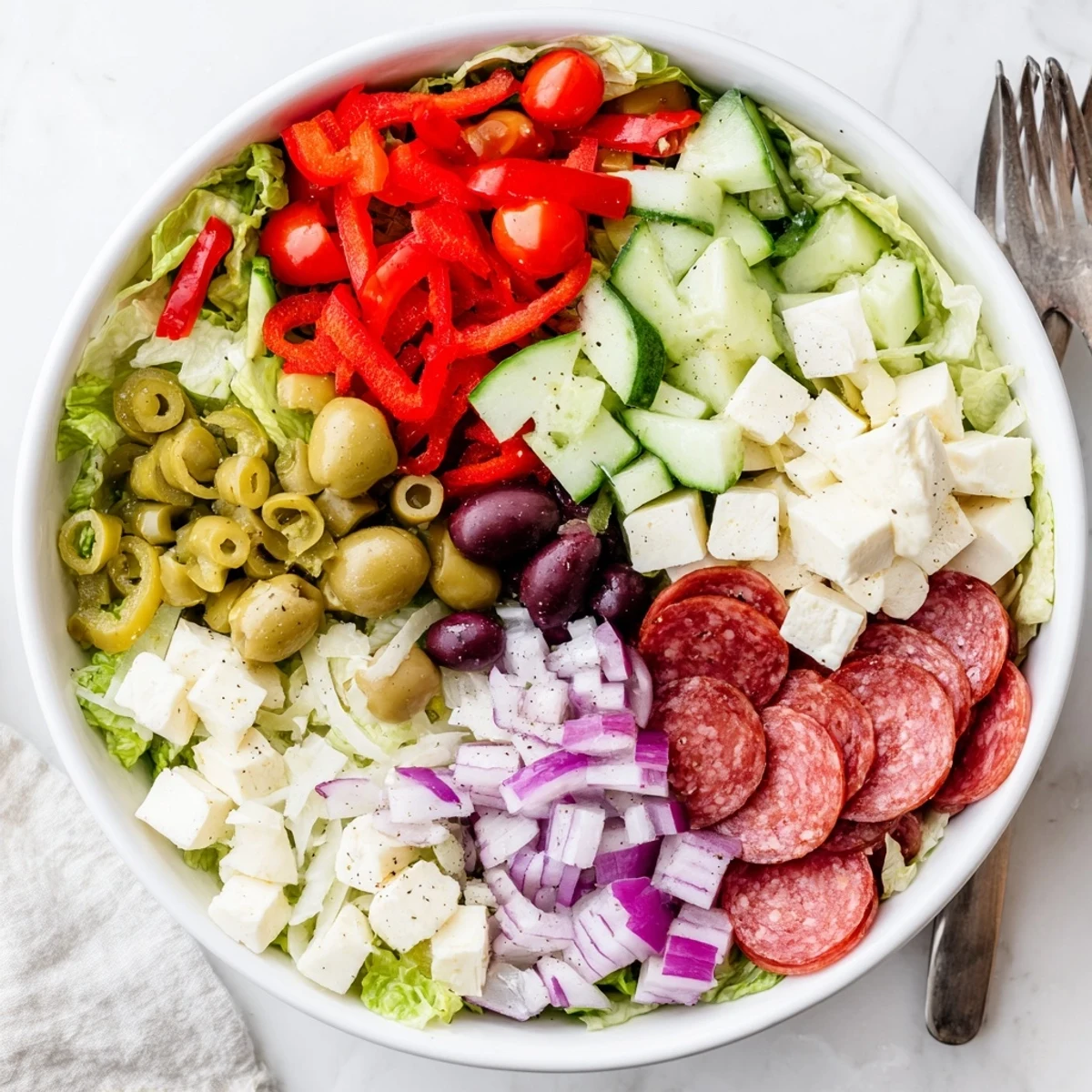 Vibrant bowl of Italian chopped salad featuring romaine, tomatoes, olives, pepperoncini, mozzarella, and salami tossed in dressing