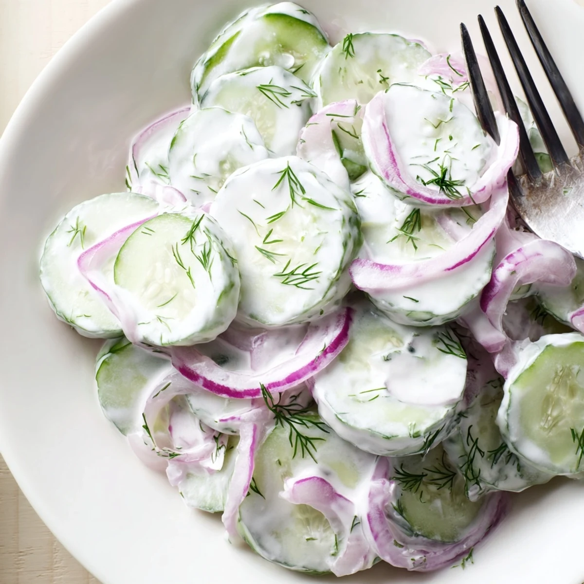 Refreshing creamy cucumber salad with thinly sliced red onions and herbs in a white bowl