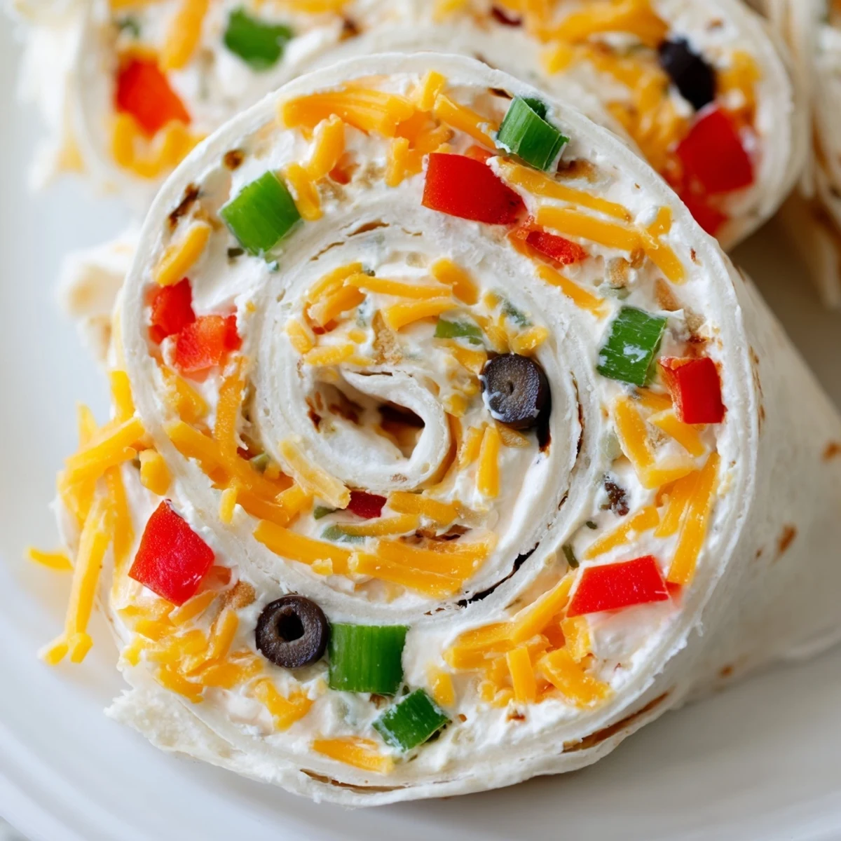 Colorful spiral of easy tortilla pinwheels filled with creamy cheese and chopped vegetables on a serving platter