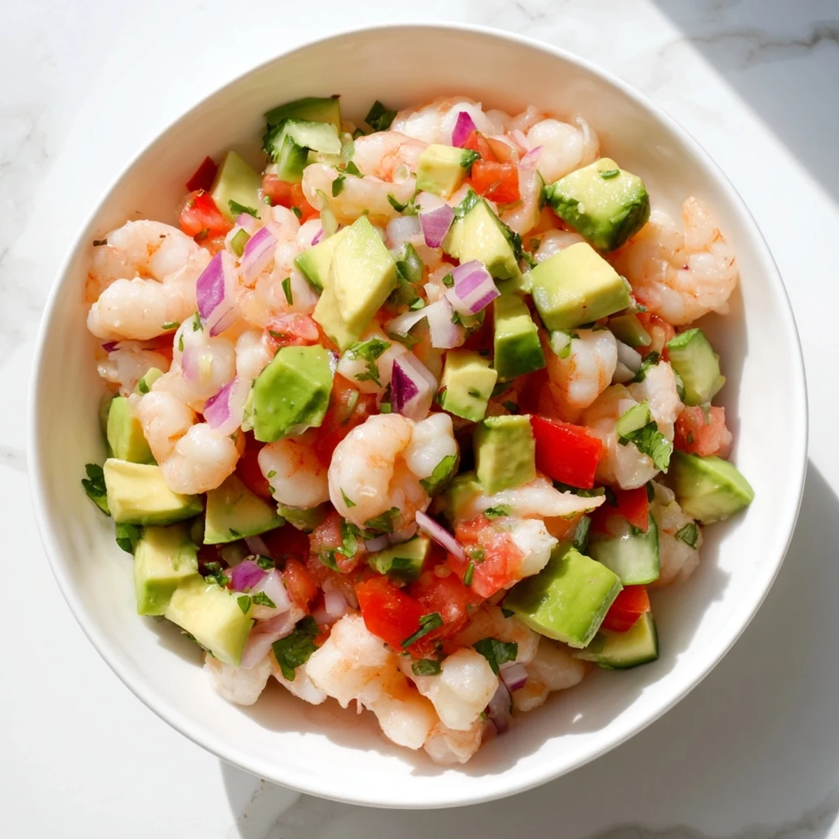 Fresh shrimp ceviche featuring diced avocado, red onion, tomatoes, and cilantro in tangy citrus juices.