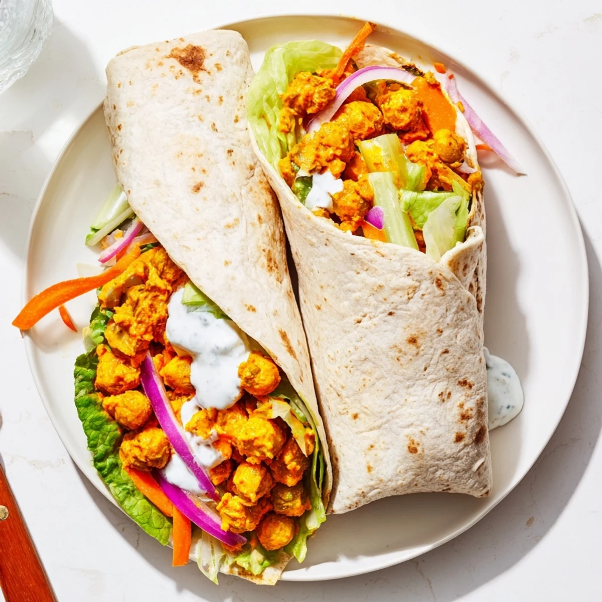 Spicy buffalo chickpea wrap rolled with fresh julienned carrots, red onion slices, and creamy ranch dressing ready for lunch