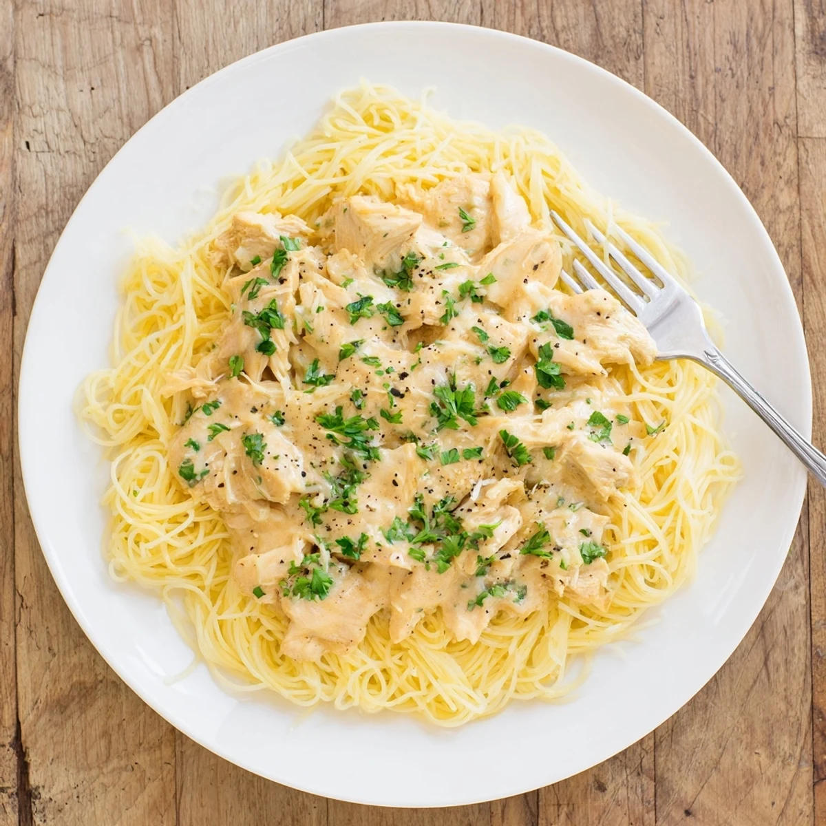 Creamy Crock Pot Angel Chicken draped over golden angel hair pasta with fresh parsley garnish
