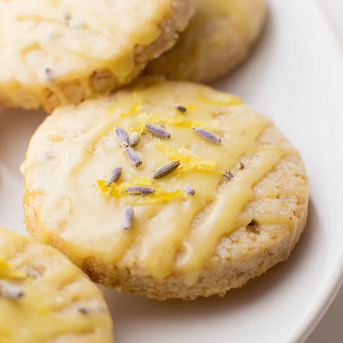 Iced Lemon Lavender Shortbread Cookies drizzled with glossy icing on a rustic white plate
