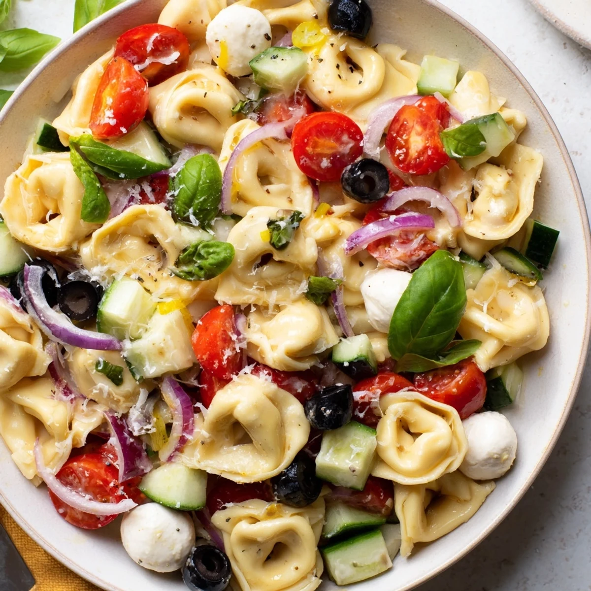 Cheese tortellini salad tossed with crisp vegetables and fresh basil on a white platter