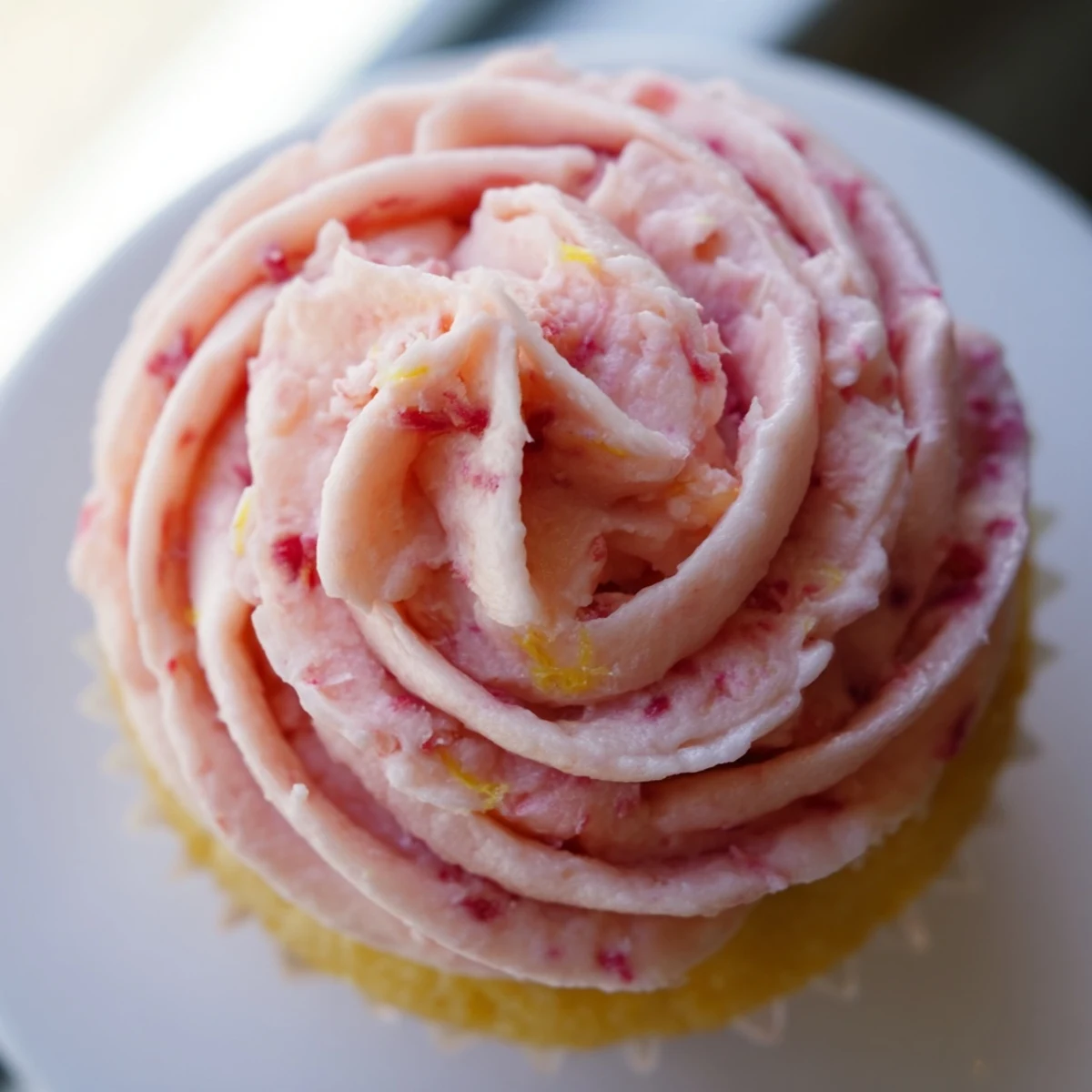 Fluffy strawberry lemonade cupcakes crowned with tangy pink frosting and bright lemon zest garnish