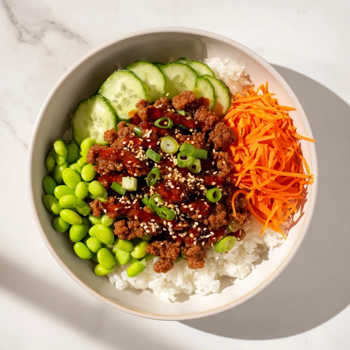 Savory hot honey ground beef bowl topped with colorful carrots cucumber and sesame seeds