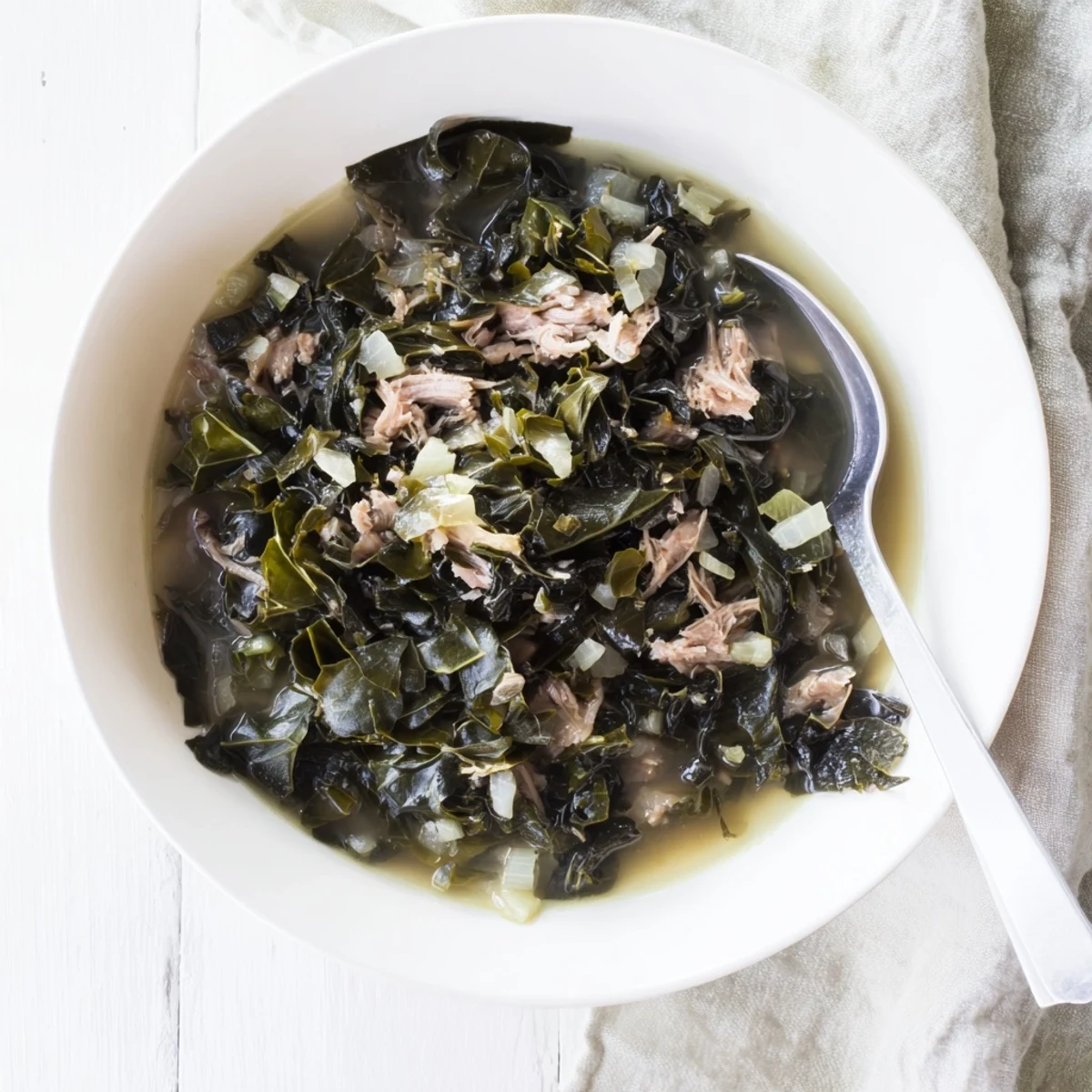 Tender braised collard greens with garlic and aromatics in dark rich cooking liquid ready to serve
