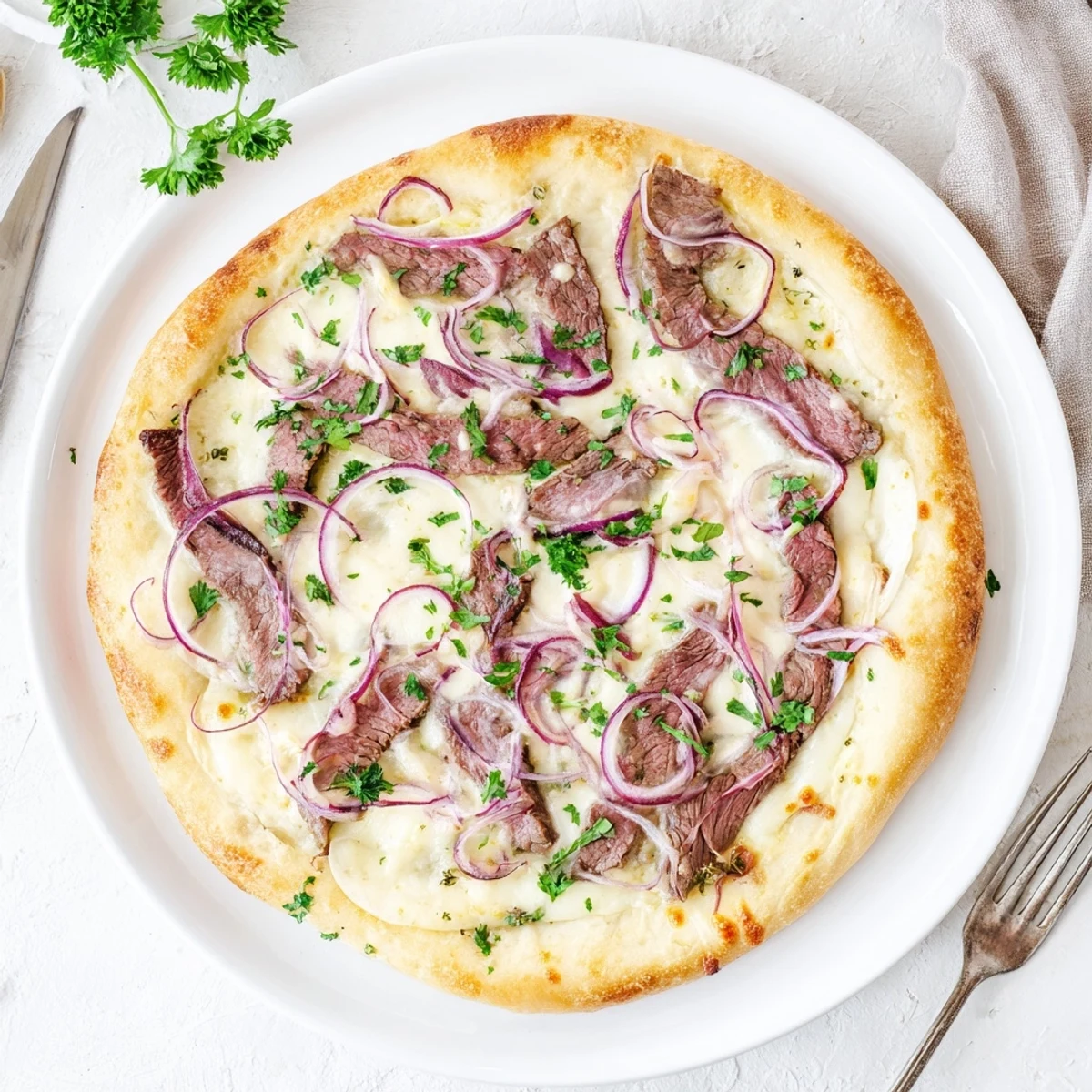 Golden Beef Alfredo Pizza topped with melted mozzarella and sliced beef on a white plate