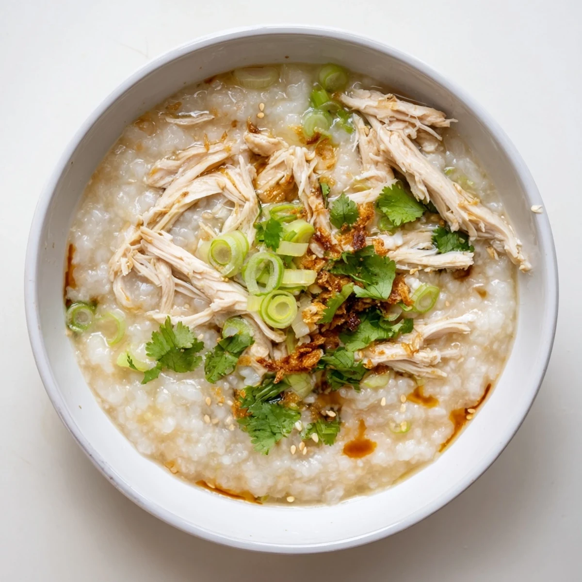 Steaming hot chicken congee porridge garnished with fresh cilantro and sesame oil drizzle