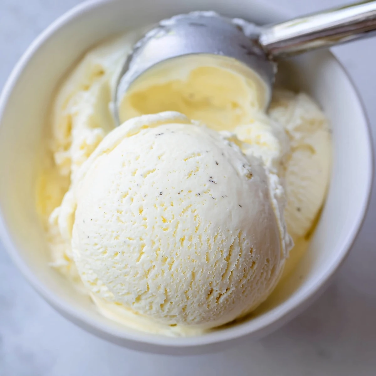 Creamy homemade vanilla ice cream scooped into a chilled glass bowl with melting texture