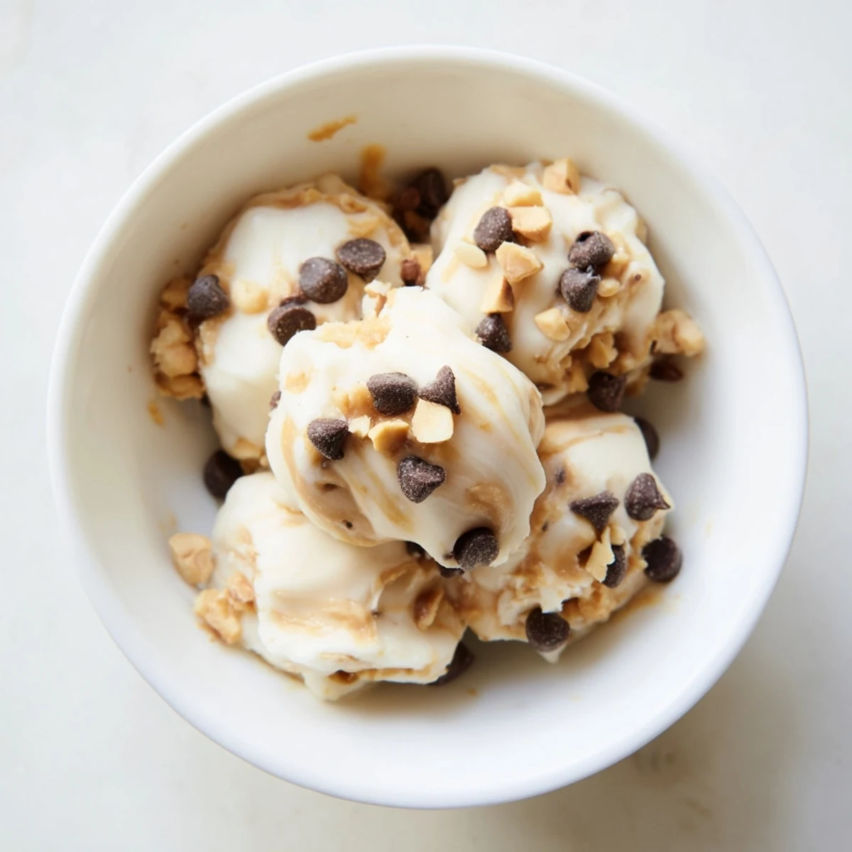Frozen peanut butter Greek yogurt bites arranged on a white plate with chocolate chip toppings