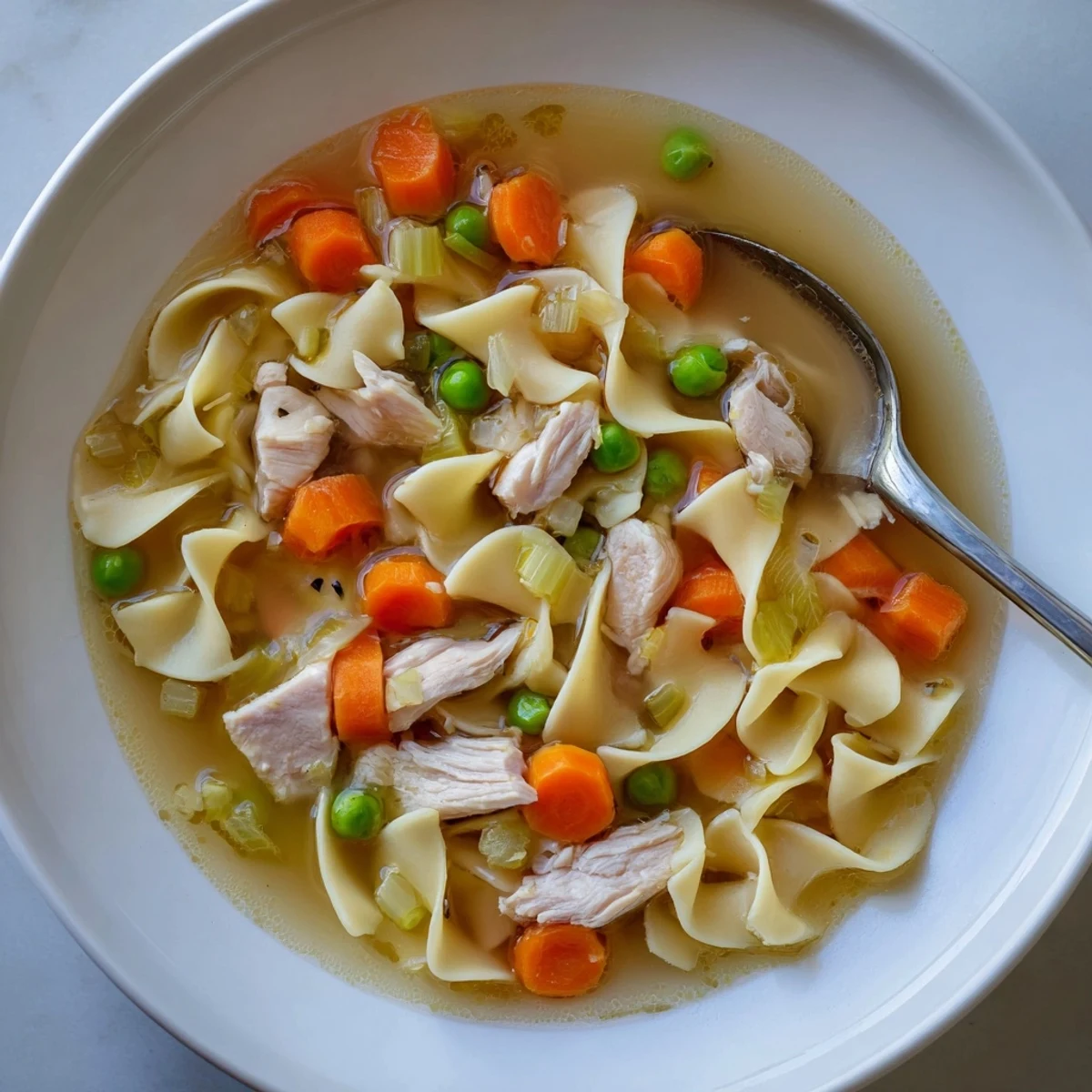 Hearty one pot chicken and noodles featuring egg noodles, peas, and sliced carrots