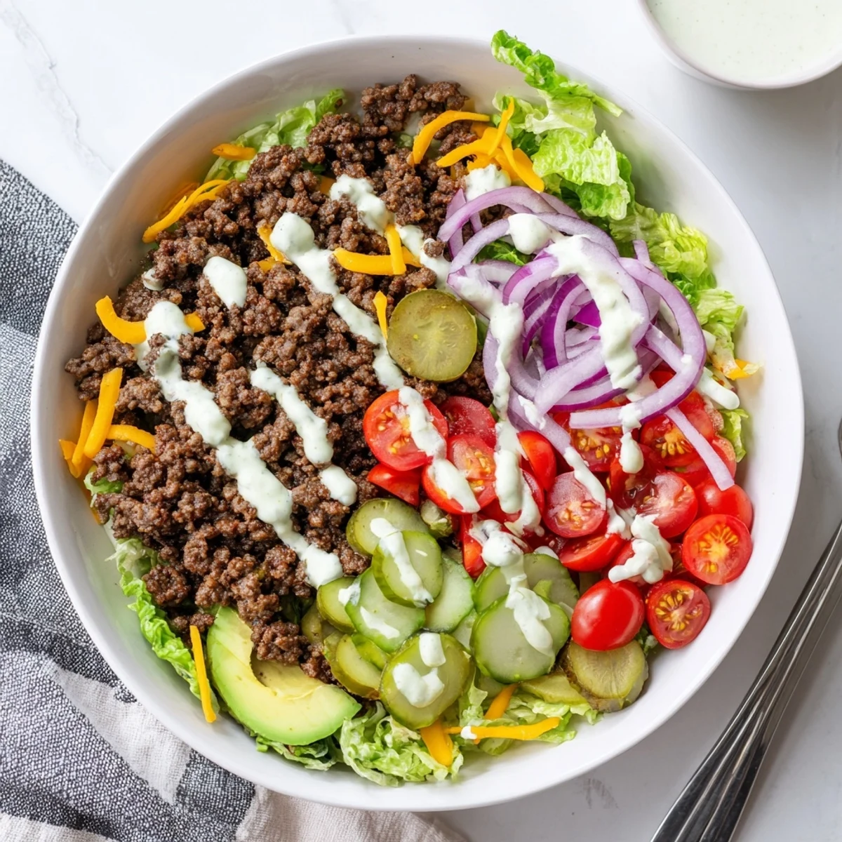 Savory protein packed burger bowls with seasoned ground beef, fresh vegetables, and tangy yogurt sauce drizzled on top