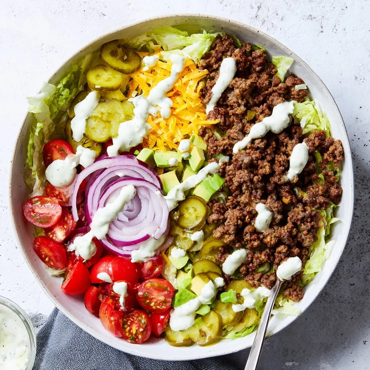 Hearty low carb protein packed burger bowls arranged with cooked meat, avocado, red onion, and zesty burger sauce