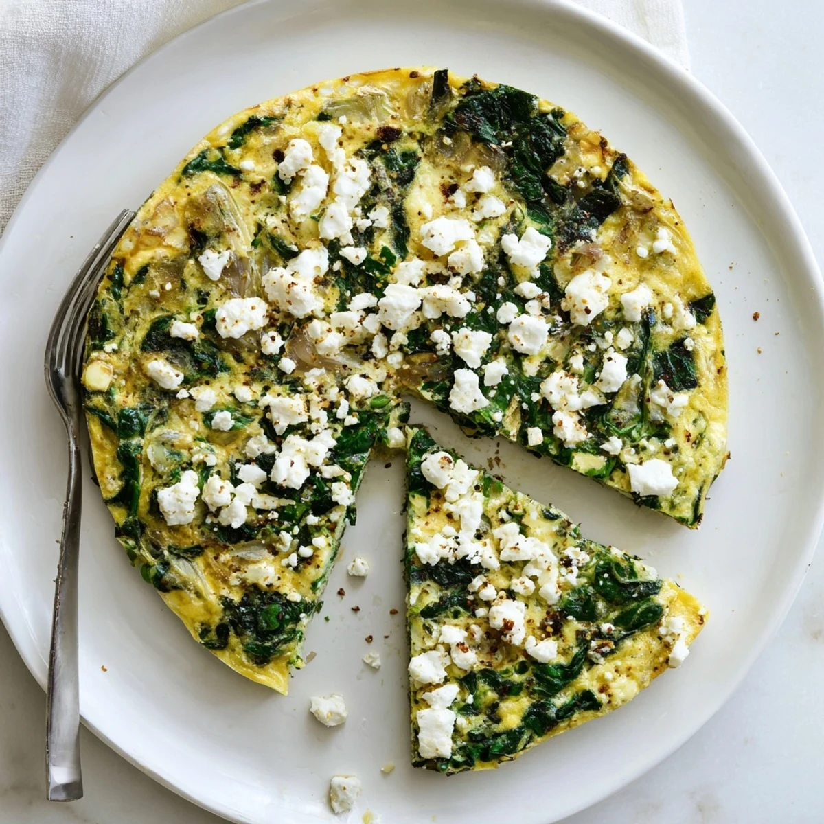 Mediterranean-style spinach frittata featuring creamy feta crumbles over a tender egg and vegetable base