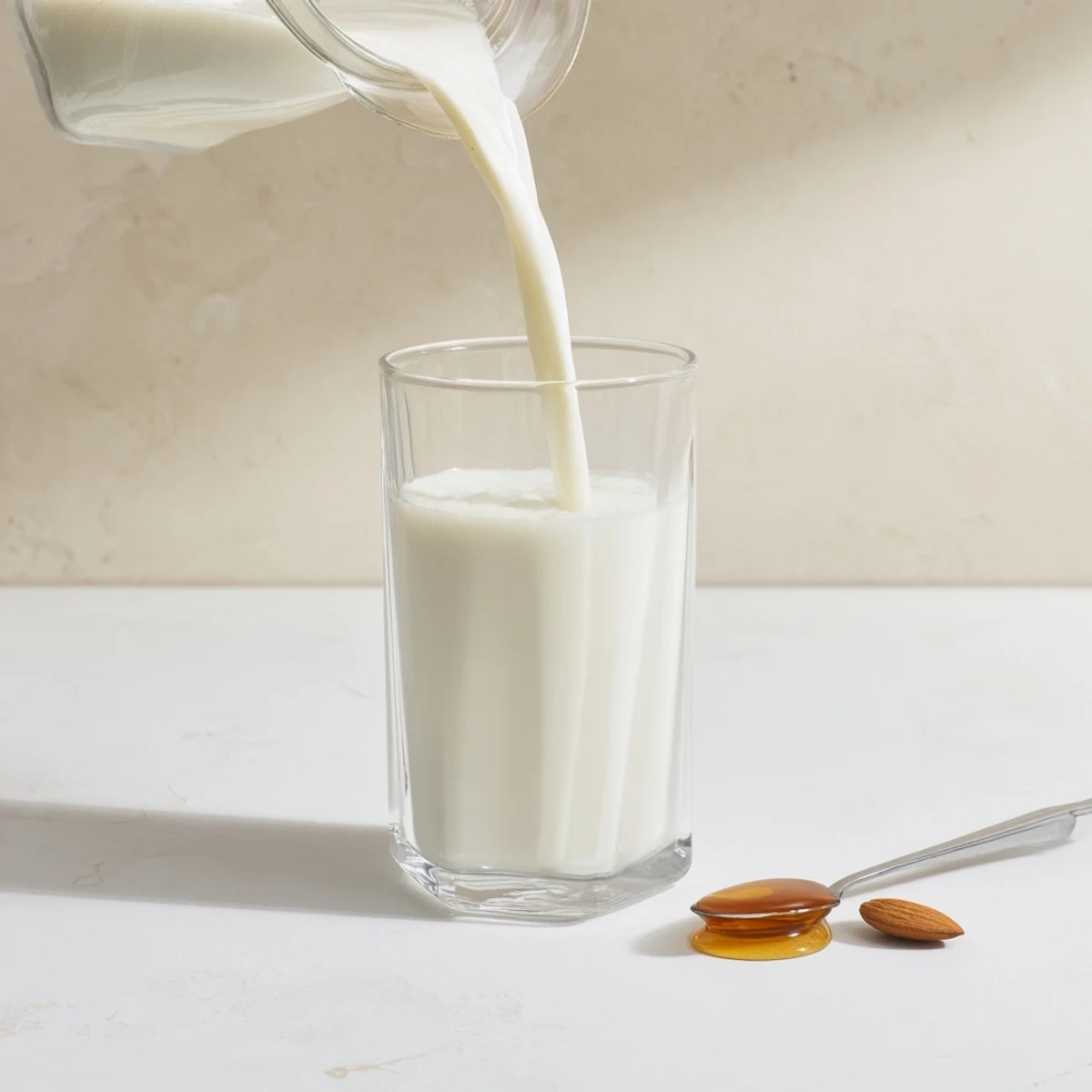 Glass jar of creamy homemade almond milk placed on wooden kitchen counter near raw almonds