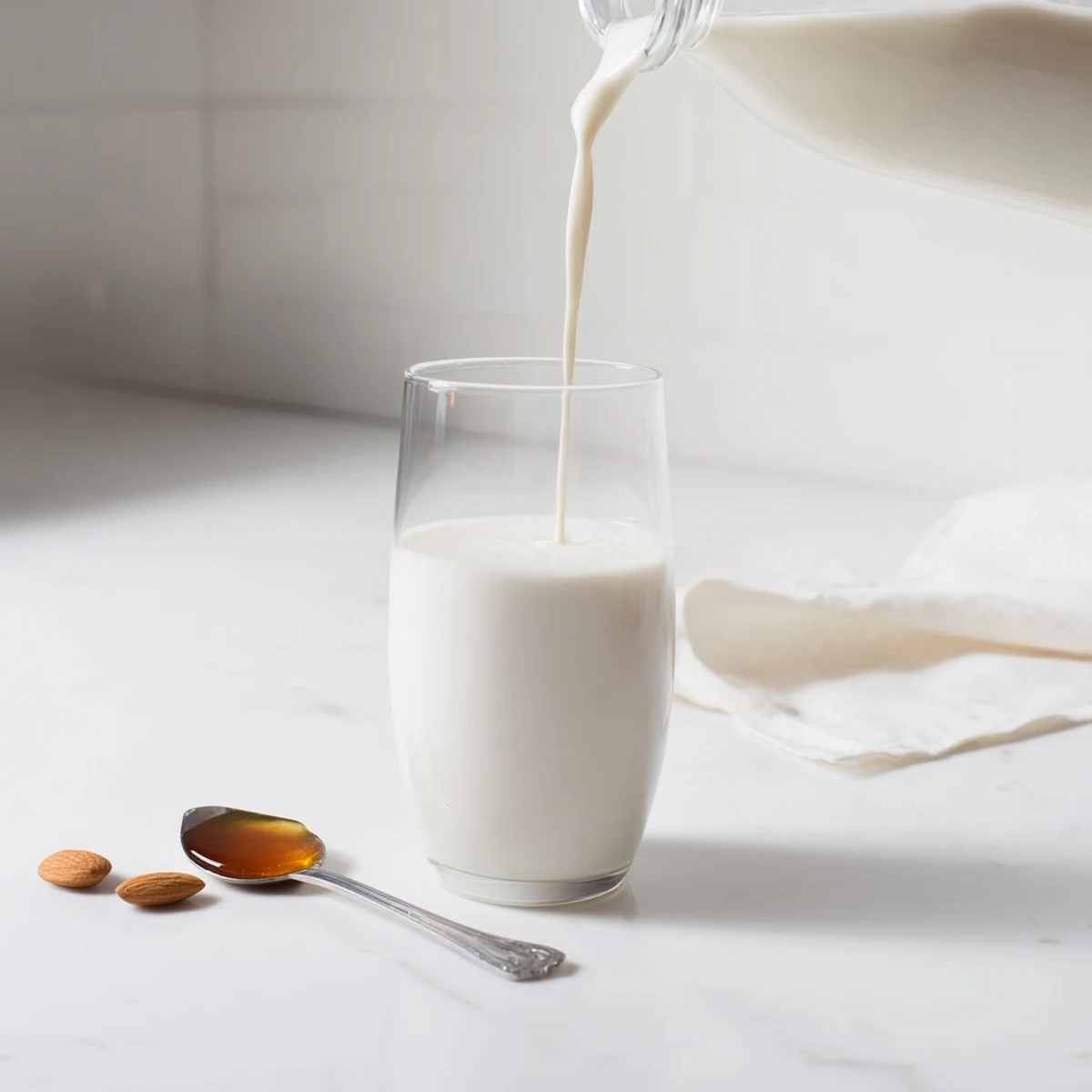 Fresh homemade almond milk poured into a clear glass showing pure white creamy texture