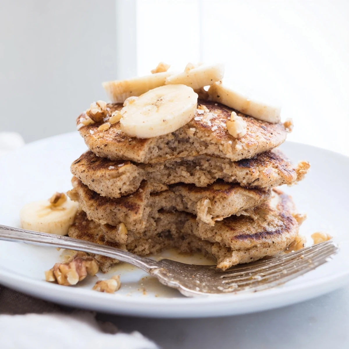 Golden stack of protein banana pancakes topped with fresh maple syrup and berries on a white plate