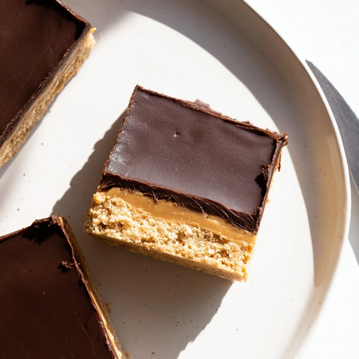 Slice of no-bake peanut butter bars showing crumbly base and glossy chocolate topping on white plate