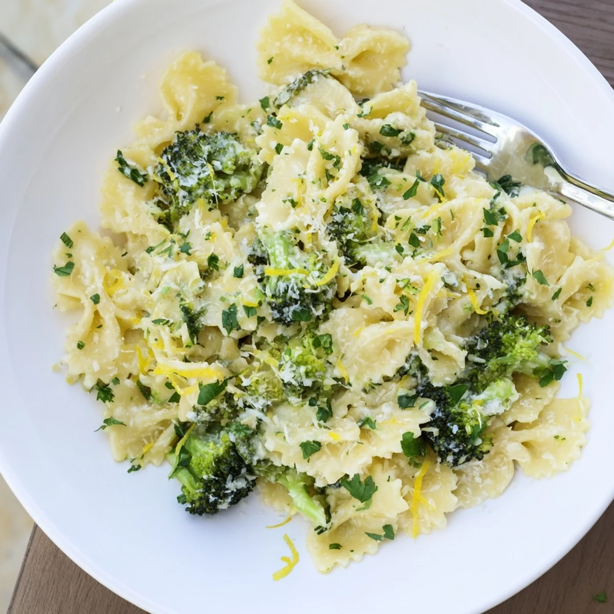 Creamy mafaldine pasta limone broccoli topped with parmesan and fresh herbs in a white bowl