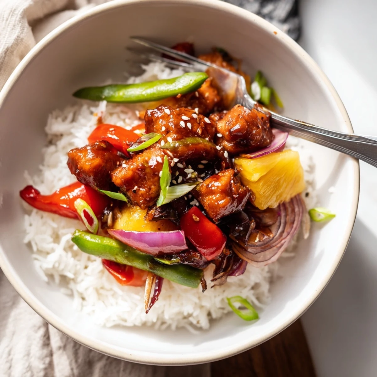 Steaming pineapple chicken rice bowl topped with crisp bell peppers and toasted sesame seeds