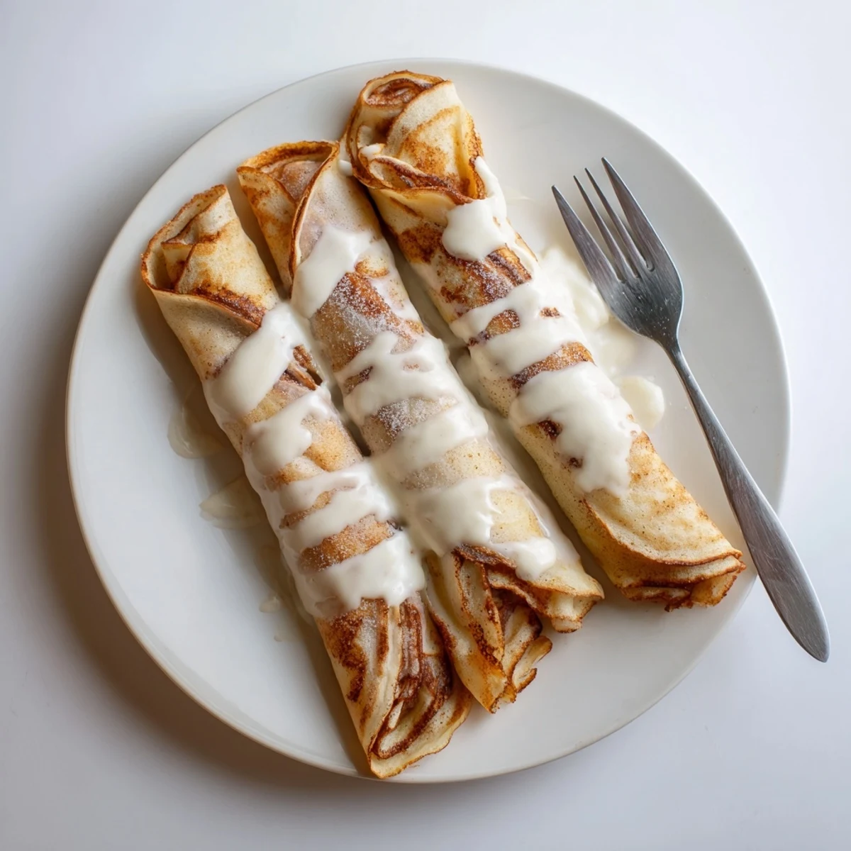 Cinnamon Roll Protein Crepes drizzled with cream cheese glaze on a warm plate