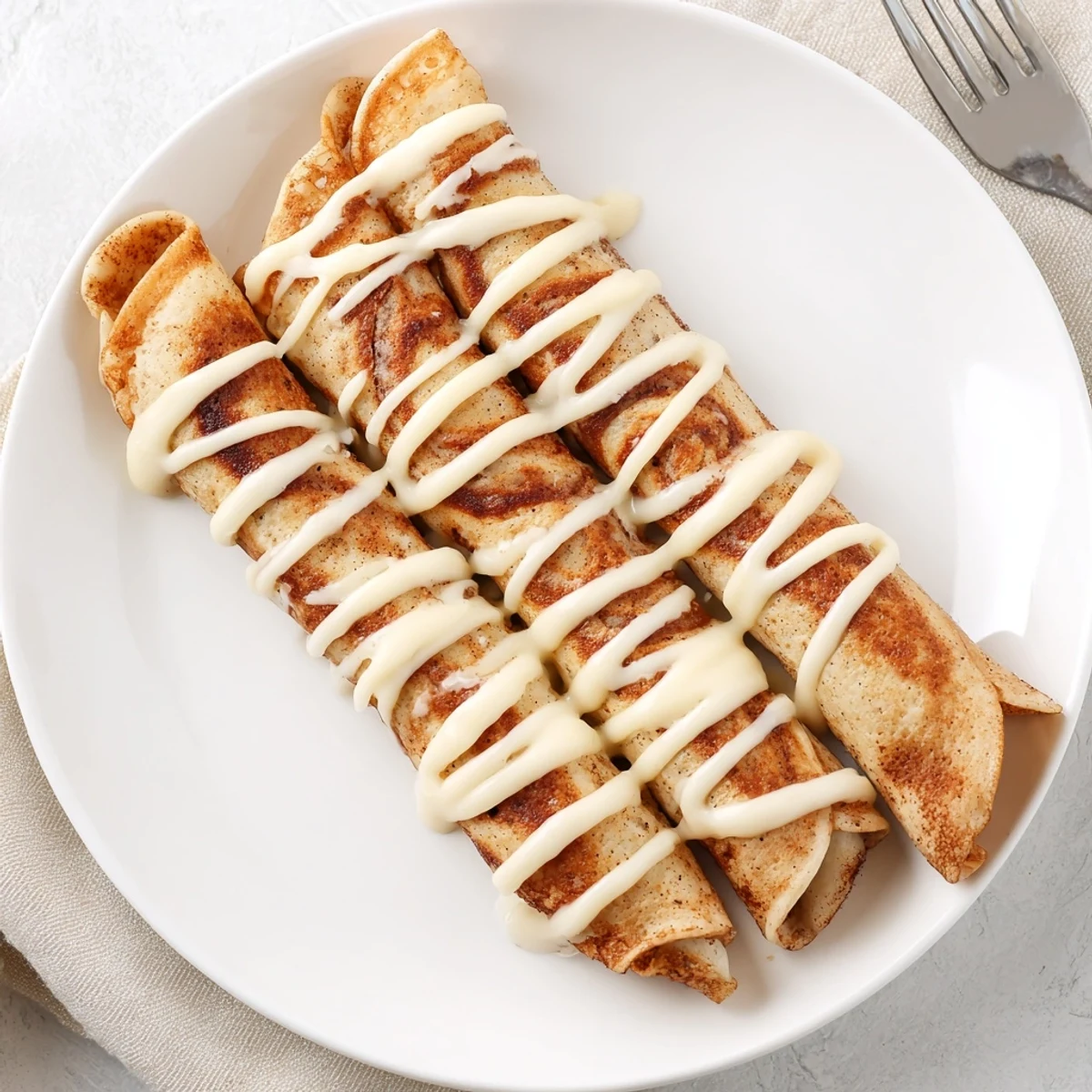 Stacked Cinnamon Roll Protein Crepes topped with luscious cream cheese icing served warm