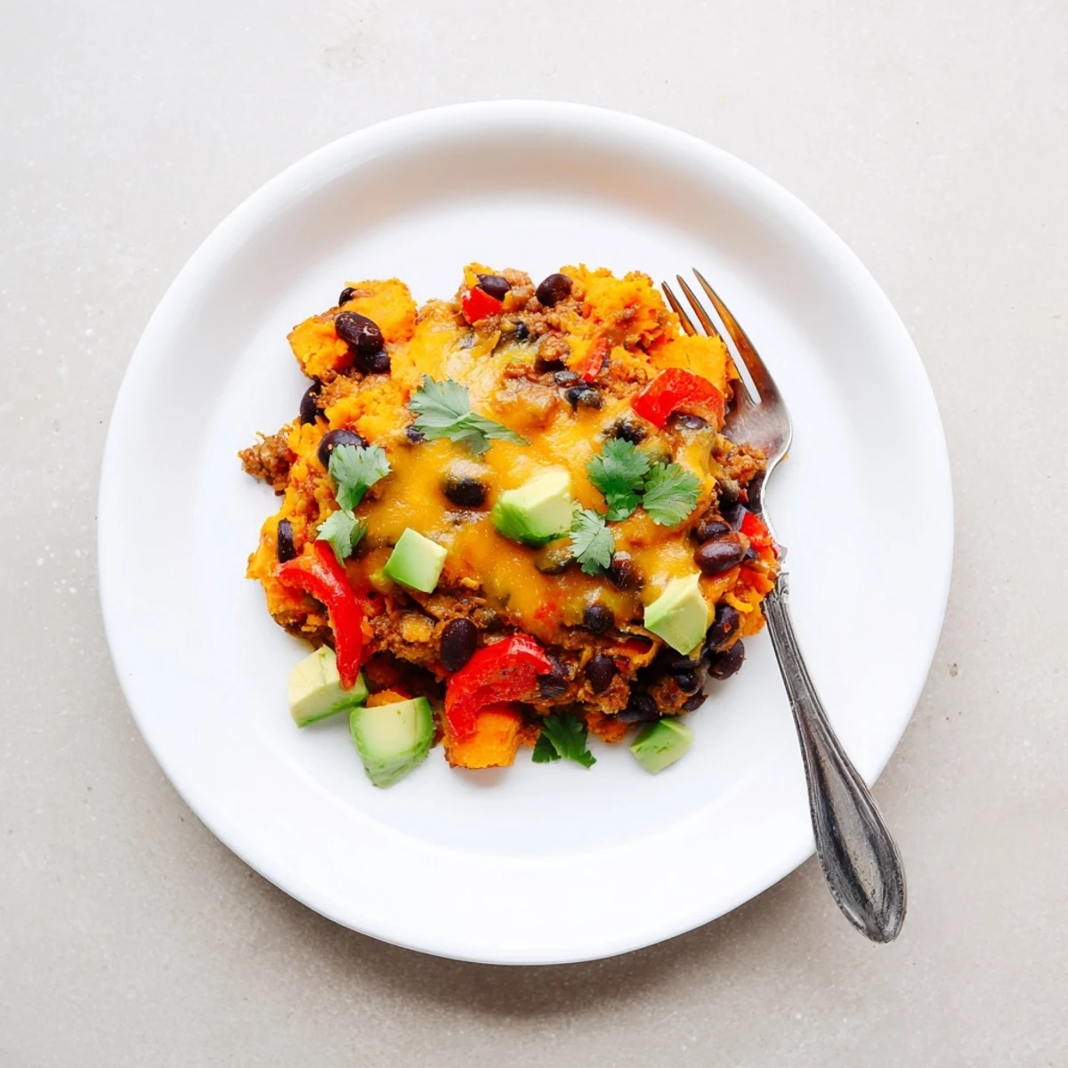 Hearty sweet potato turkey black bean bake scooped into a bowl garnished with sliced avocado
