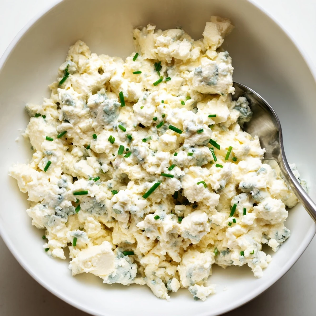 Thick blue cheese dip topped with crumbled cheese and chopped chives on a wooden board