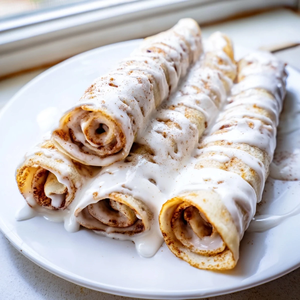 Thin cinnamon roll protein crepes rolled with creamy cinnamon filling and drizzled with sweet vanilla glaze