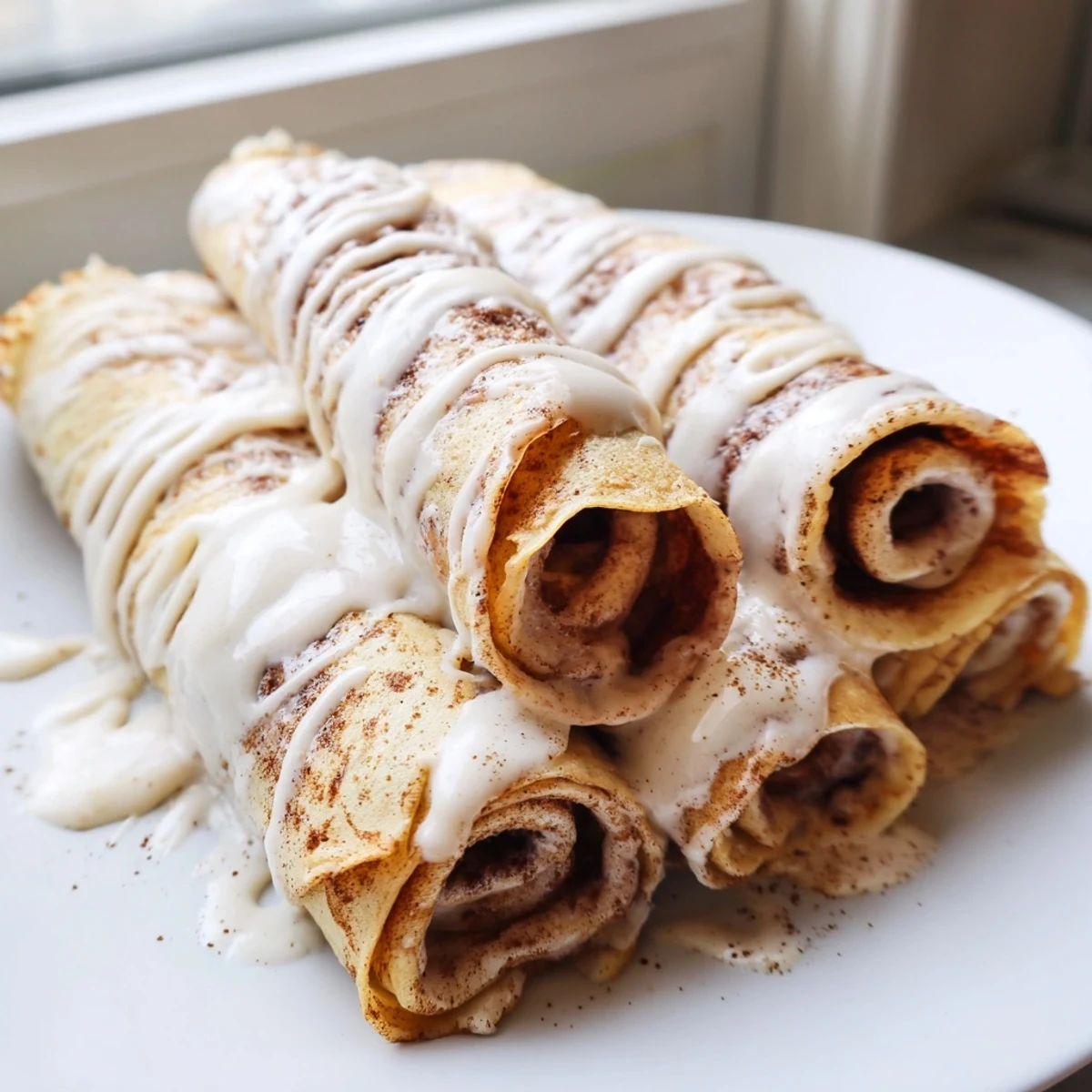 Golden cinnamon roll protein crepes stacked on a plate topped with cream cheese swirl