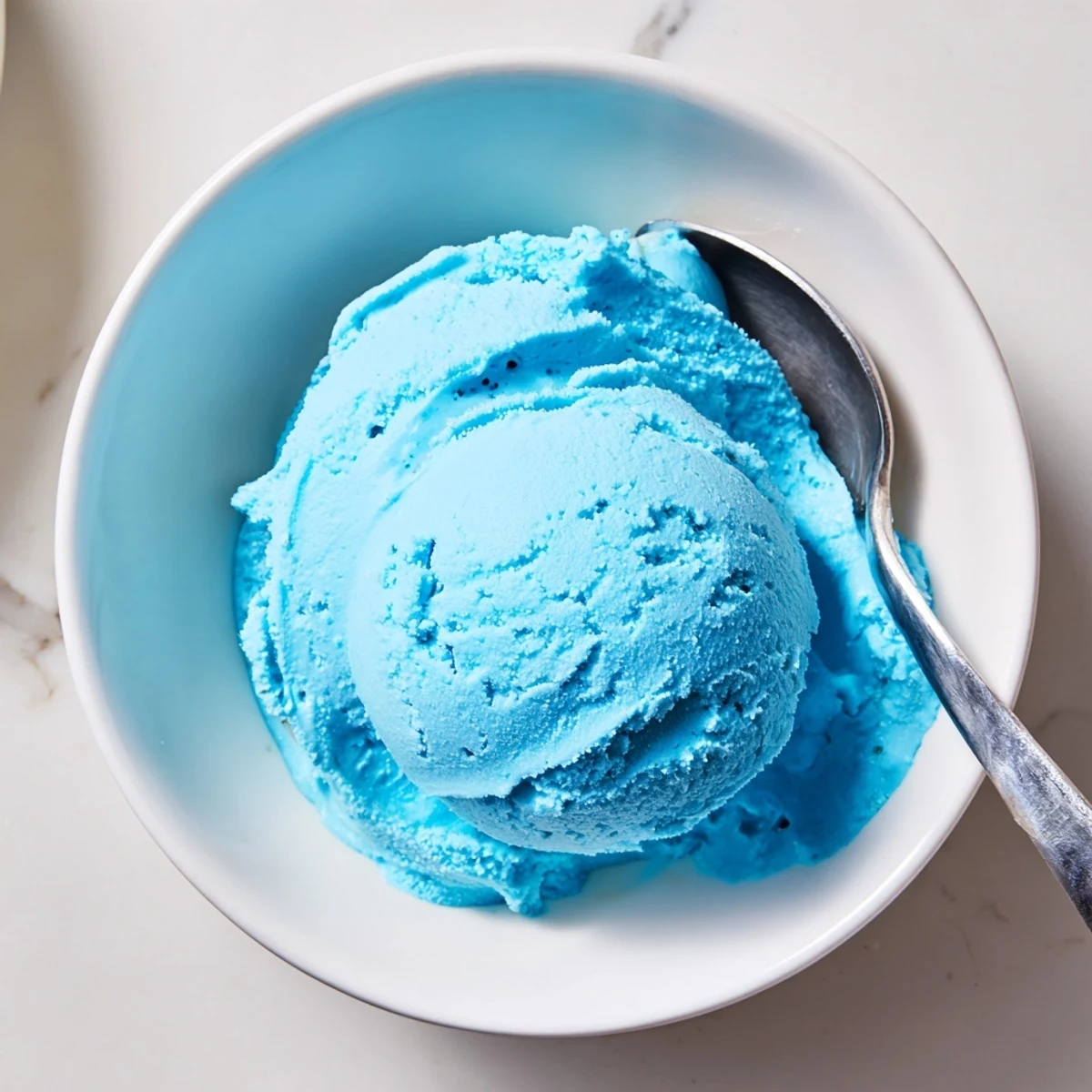 Vibrant blue moon ice cream with a smooth velvety texture garnished with fresh raspberries