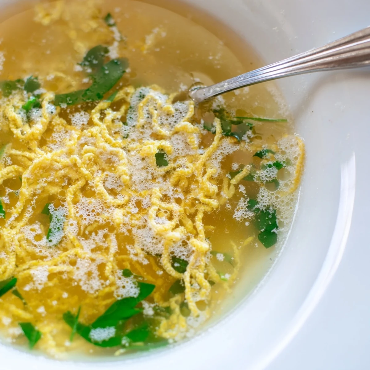 Steaming bowl of Stracciatella Soup with delicate egg ribbons and wilted fresh spinach