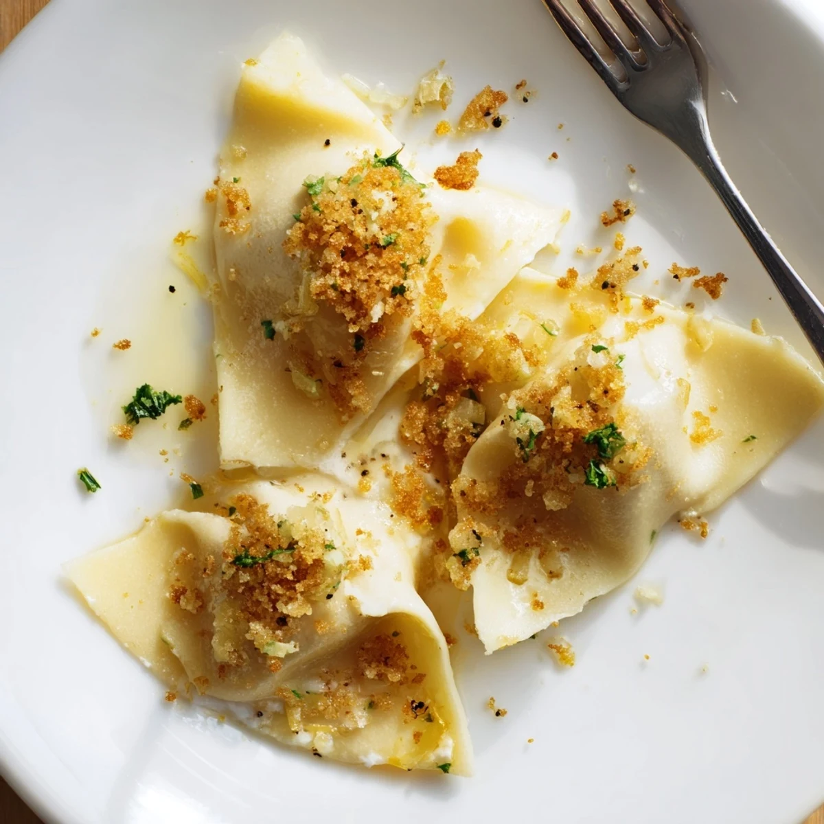 Creamy leek burrata triangoli plated on a white dish with herb-flecked golden crumbs