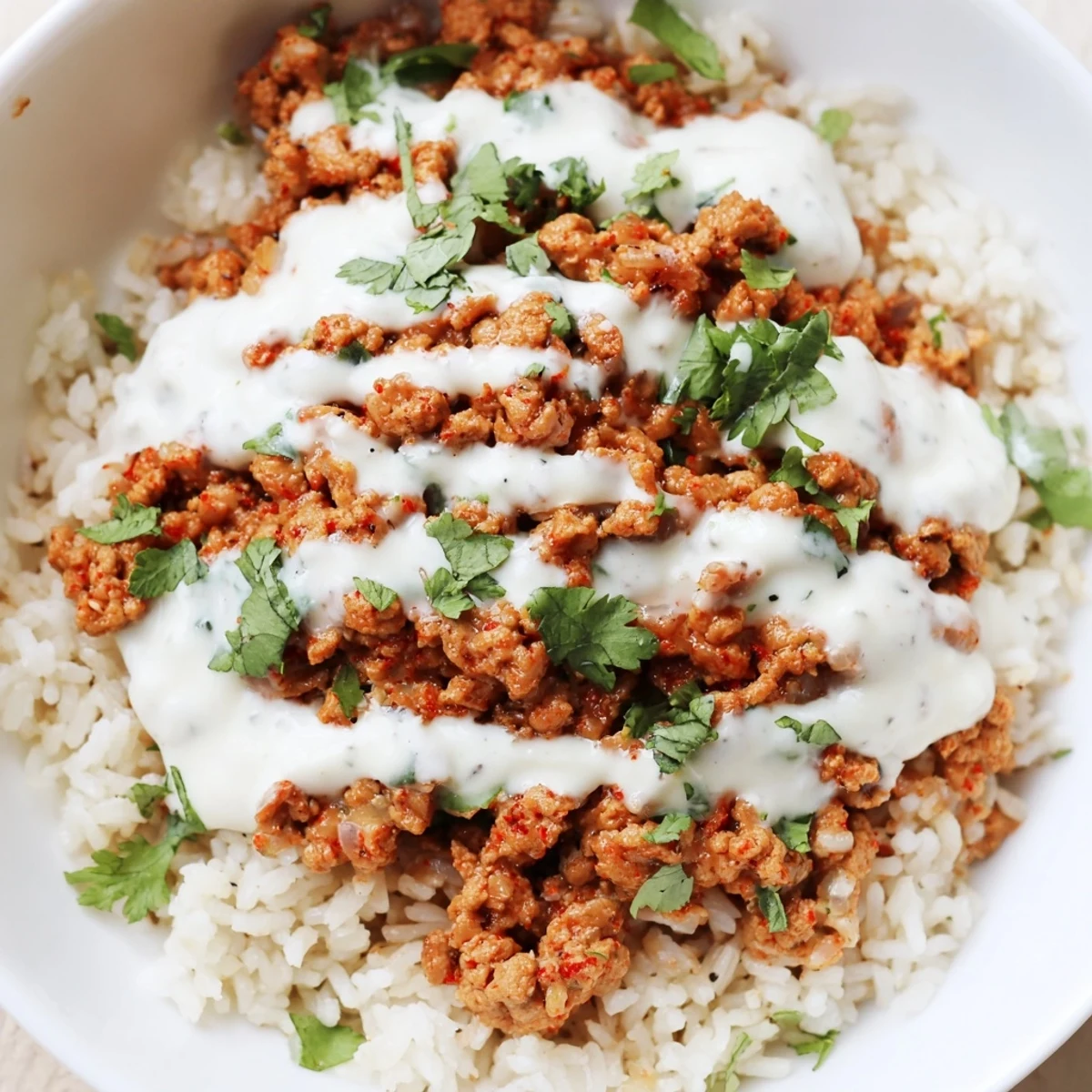 A warm spiced turkey rice bowl topped with crunchy fresh vegetables and creamy yogurt sauce drizzled on top