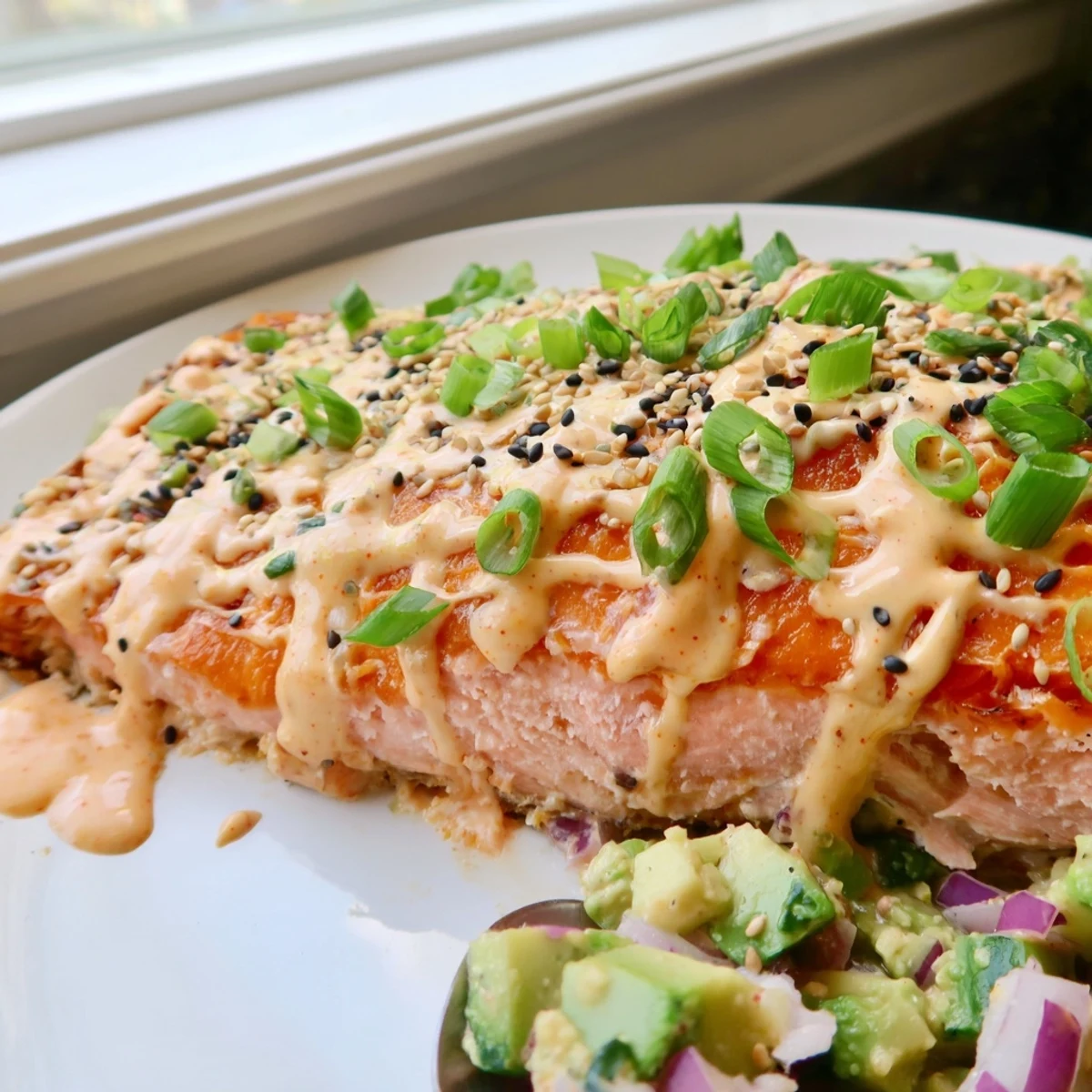 Spicy Bang Bang Salmon drizzled with sauce beside fresh green avocado cucumber salsa
