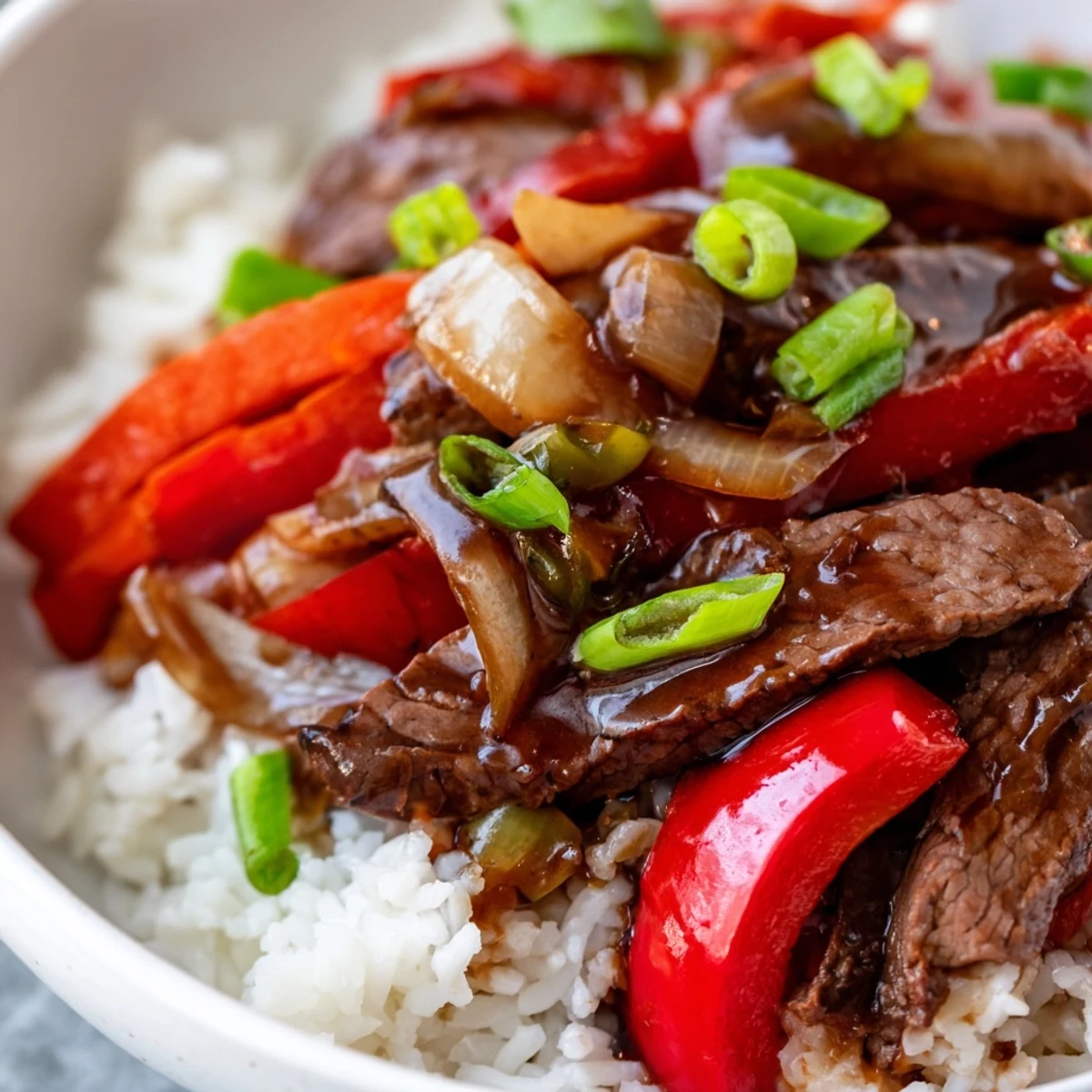 Glossy strips of Slow Cooker Pepper Steak served over fluffy white rice with green onions