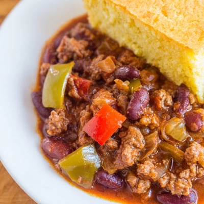 Two slices of golden cornbread rest next to a hearty ladle of Beef and Bean Chili with beans and tender beef.